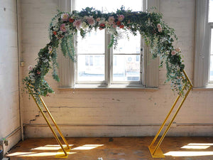 gold double hexagonal wedding arch in front of a window